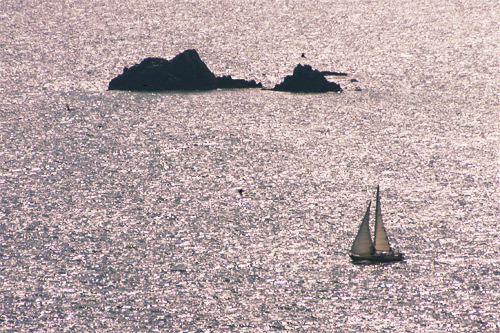 Photographie d'un voilier slalomant entre les roches bretonnes